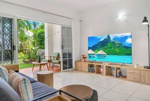 A living room with a large flat-screen TV, a sofa, a coffee table, and a TV stand with books and decorative items.