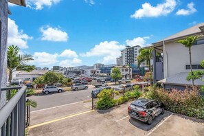 A parking lot with cars, a building with a balcony, and a clear sky.