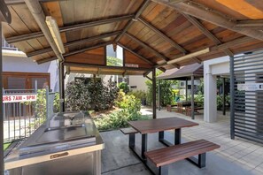 Un espacio de comedor al aire libre con techo cubierto, estación de parrilla y zona de recepción.