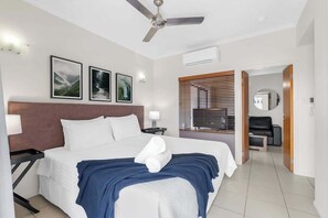 A hotel room with a bed, ceiling fan, framed pictures, and a view of the outside.