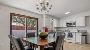 A dining area with a wooden table and chairs, a chandelier, and a view of the outdoors through a sliding glass door. - Large 4BR Villa Near Heated Pool | Solana 1 (Tucson)