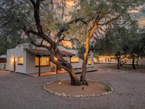 A modern building with a white exterior and a tiled roof, surrounded by trees and a gravel courtyard. - Large 4BR Villa Near Heated Pool | Solana 1 (Tucson)