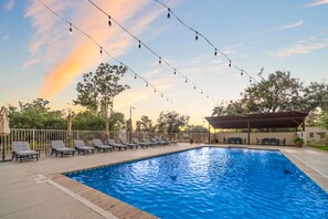 A swimming pool with lounge chairs and string lights, surrounded by trees and a covered seating area. - Large 4BR Villa Near Heated Pool | Solana 1 (Tucson)