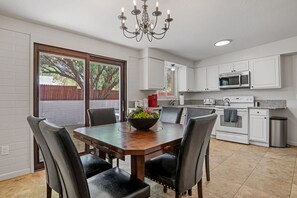 A dining area with a wooden table and chairs, a chandelier, and a view of the outdoors through a sliding glass door. - Large 4BR Villa Near Heated Pool | Solana 1 (Tucson)