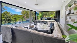 Ein moderner Außenbereich mit einer Couch, einem Esstisch und Stühlen, mit Blick auf ein Schwimmbecken und Grünflächen.