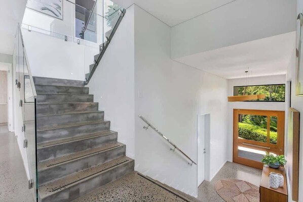 A modern interior with a staircase, a glass railing, and a wooden door leading outside.