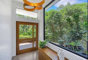 Un interior moderno con un ventanal grande, una puerta de madera y una planta sobre una consola de madera.