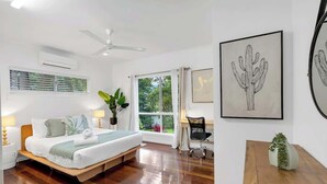 A bedroom with a bed, bedside tables, a desk, a chair, a window with curtains, and artwork on the walls. - Tropical Refuge—Classic Queenslander Paradise (Aeroglen)