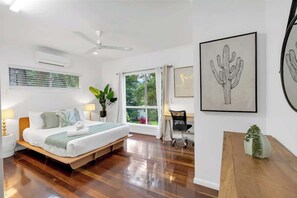 Une chambre à coucher comprenant un lit, des tables de chevet, un bureau, une chaise, une fenêtre avec des rideaux et des œuvres d’art accrochées aux murs.