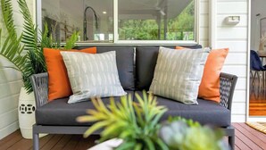 A dark grey sofa with patterned cushions, a potted plant, and a view through a large window. - Tropical Refuge—Classic Queenslander Paradise (Aeroglen)