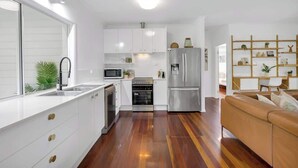 A modern kitchen with white cabinetry, stainless steel appliances, and a wooden floor. - Tropical Refuge—Classic Queenslander Paradise (Aeroglen)