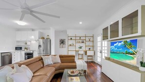 A modern living room with a brown leather sofa, a glass coffee table, and a TV displaying a beach scene. - Tropical Refuge—Classic Queenslander Paradise (Aeroglen)