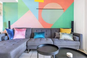 A modern living room with a grey sectional sofa, a black coffee table, and a colorful abstract wall art.