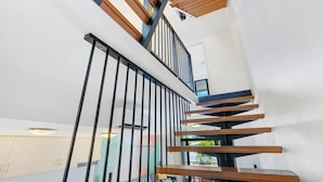 A modern staircase with wooden steps and black railings, leading to an upper floor. - The Loft—Trendy Coastal Charm with Pool (Cairns North)