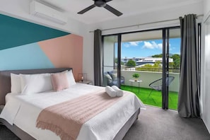 Camera d'albergo con letto, ventilatore a soffitto, balcone con vista e un piccolo tavolo con una sedia.