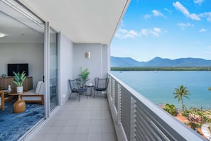 Un balcone con vista su un lago e montagne, una TV, un divano e un piccolo tavolo con sedie.