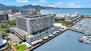 Un hotel moderno con diversi piani, una marina piena di barche e vista sul mare e sulle montagne.