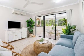 A living room with a sofa, TV, and a dining area with chairs and plants.