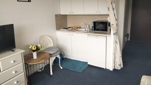 A compact kitchen with white cabinets, a microwave, a sink, and a small dining area with a chair and table.