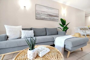 A modern living room with a grey sofa, a round wicker coffee table, and a large plant.