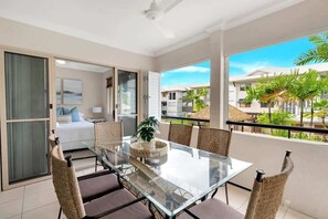 A balcony with a glass table, wicker chairs, and a view of a residential area.