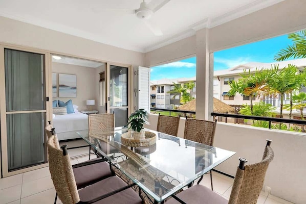Un balcon avec une table en verre, des chaises en osier et une vue sur un quartier résidentiel.