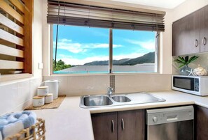 A kitchen with a window view, stainless steel sink, microwave, and wooden cabinets.