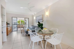 A modern dining area with a glass table, white chairs, and a view to the outside.