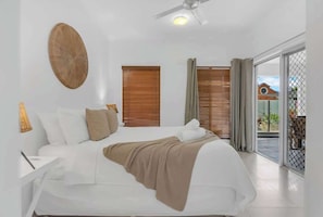 Una camera da letto con un letto, una ventola a soffitto, una lampada a parete e una finestra con tende.