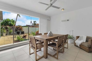 Zona pranzo con tavolo e sedie in legno, ventilatore a soffitto e vista su un patio esterno attraverso una porta in vetro.
