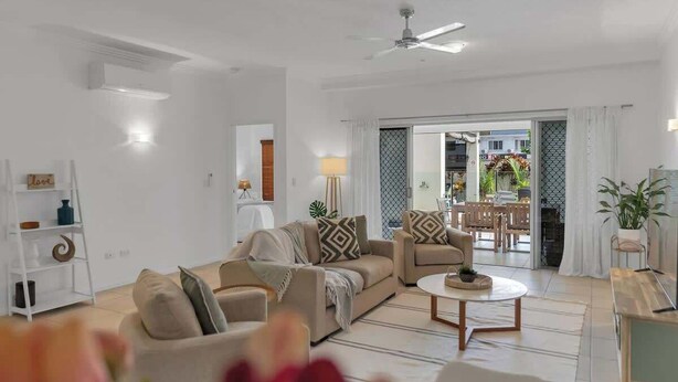 A spacious living room with a sofa, armchairs, a coffee table, and a ceiling fan.