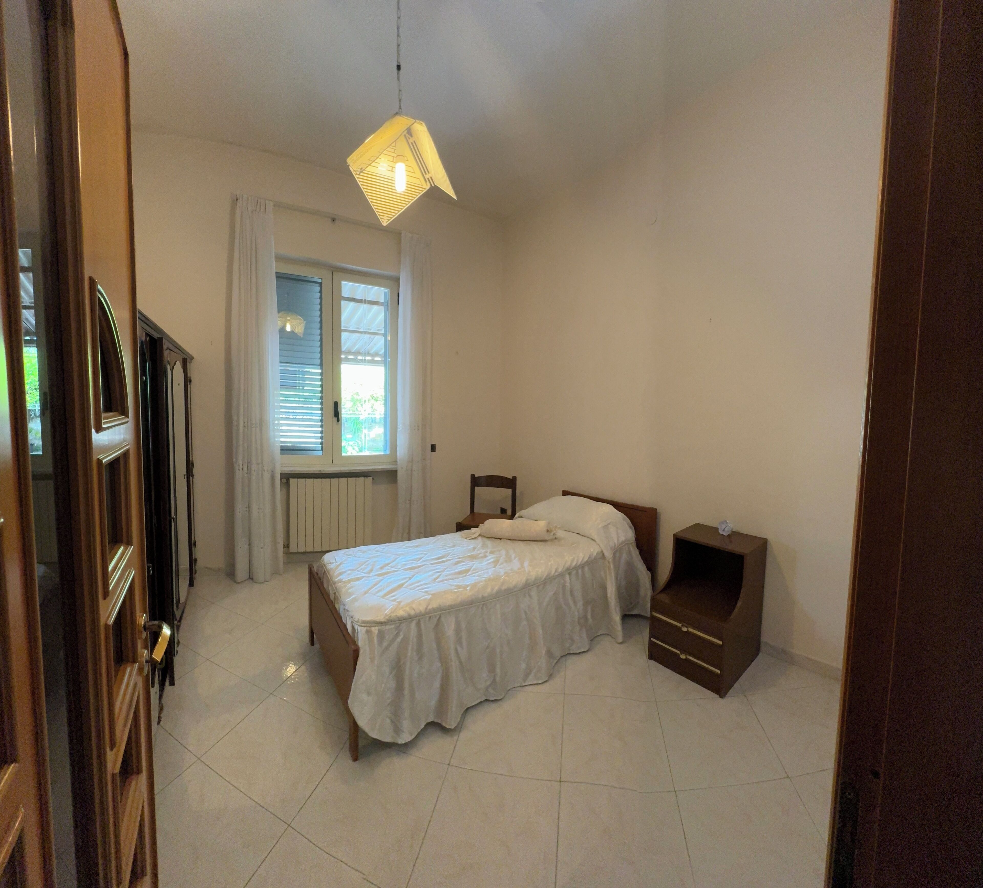 Una camera da letto con un letto, un comodino, una finestra con tende e una porta.