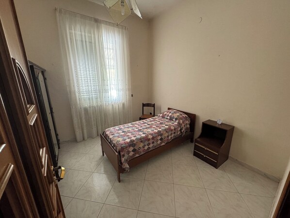 A bedroom with a bed, a nightstand, a wooden wardrobe, and a window with sheer curtains. - Casa signorile Marianna (Camposano)