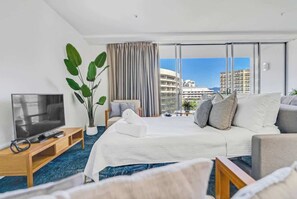 A hotel room with a bed, a TV, a plant, and a view of buildings.