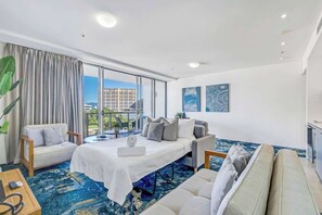 A hotel room with a bed, two sofas, a coffee table, and a large window with a view of buildings.