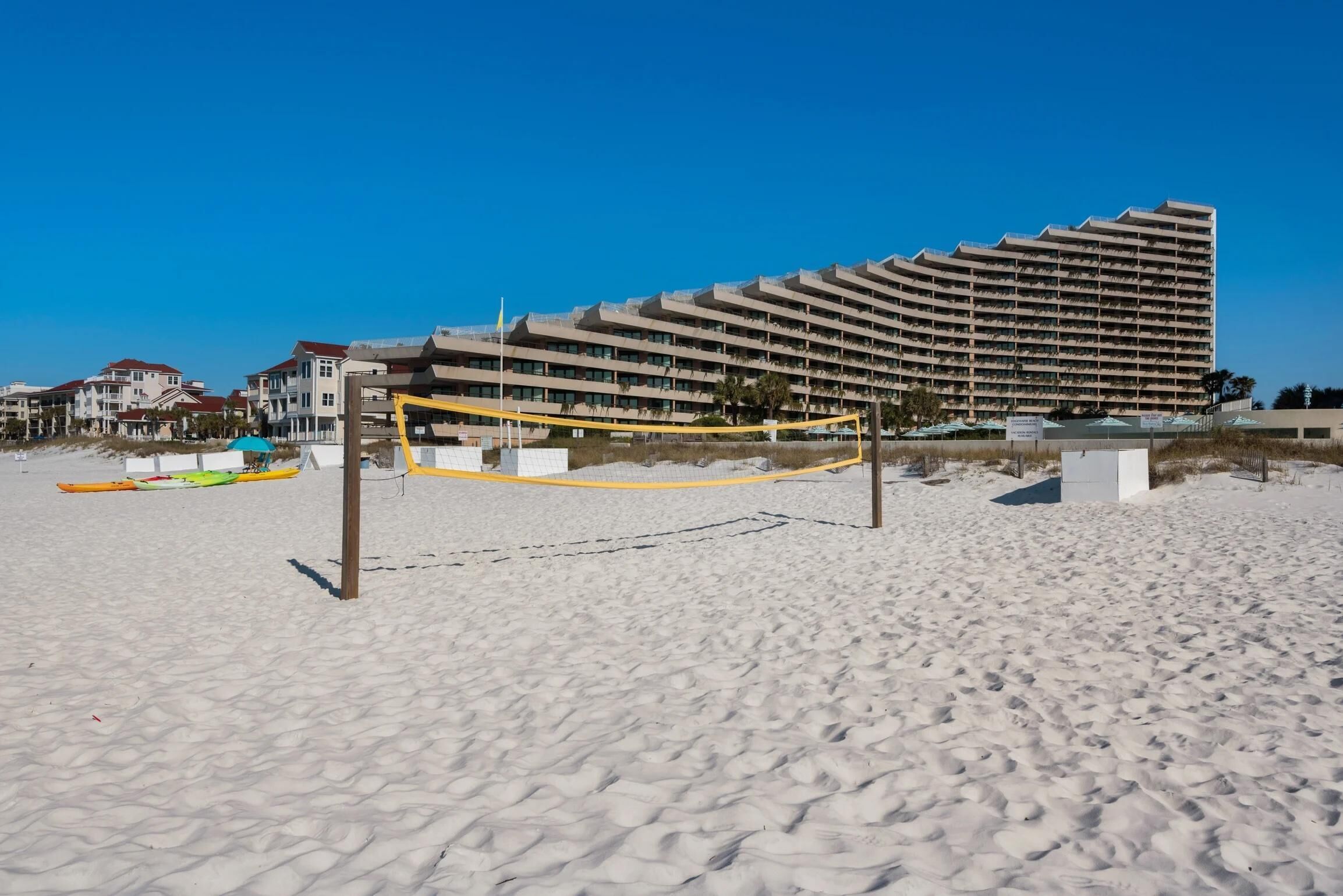 Hotel à beira-mar com fachada curva, praia arenosa em primeiro plano e caiaques alinhados.