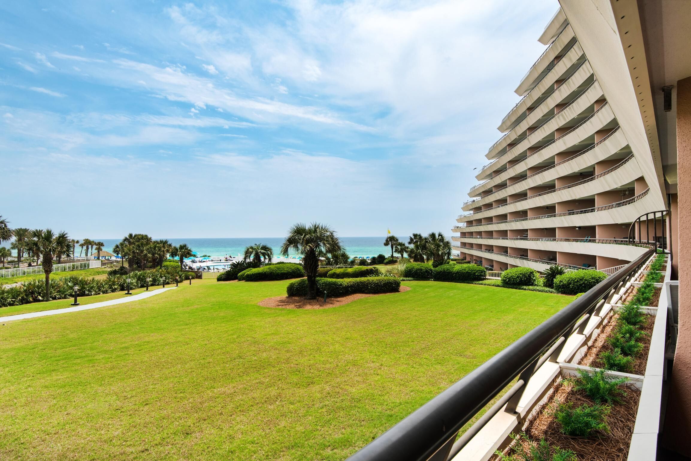 A hotel with a view of the ocean, a well-maintained lawn, and a multi-story building with balconies.