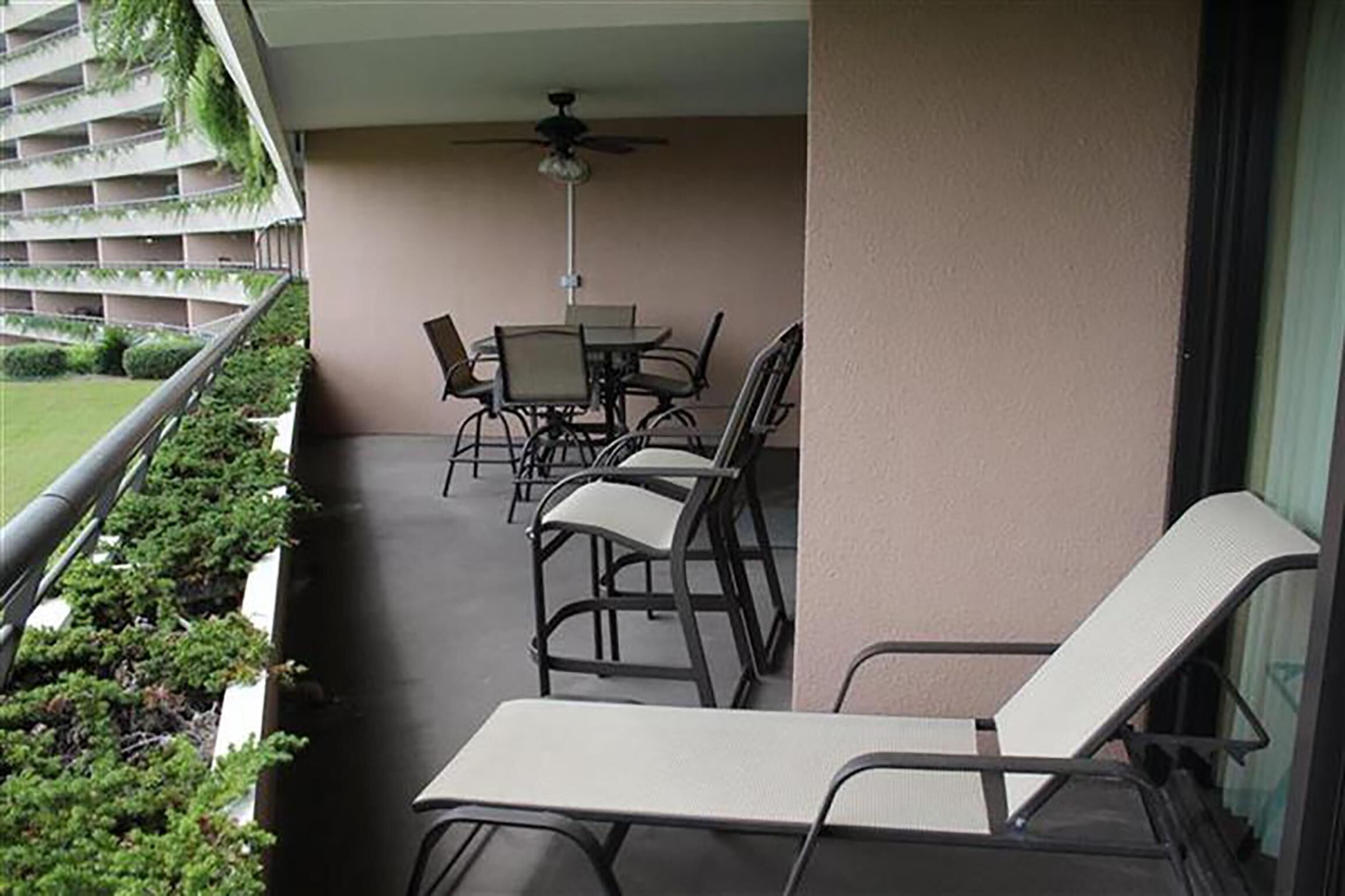 Un balcon avec une table et des chaises, un ventilateur de plafond et une vue sur un immeuble doté de balcons.