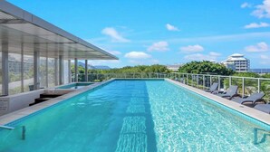 A rooftop swimming pool with clear blue water, a glass balustrade, and lounge chairs. - City Living at Harbour Lights on the Waterfront (Cairns)