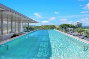 A rooftop swimming pool with clear blue water, a glass balustrade, and lounge chairs.