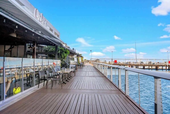 A wooden deck with outdoor seating, a glass railing, and a view of the water.