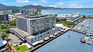 A modern hotel with multiple floors, a marina with boats, and a view of the sea and mountains. - City Living at Harbour Lights on the Waterfront (Cairns)