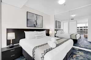 Une chambre d’hôtel avec un grand lit, une table de chevet, une lampe, un miroir et des œuvres d’art accrochées au mur.