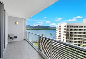A balcony with a view of a lake and mountains, a chair, and a building with balconies.