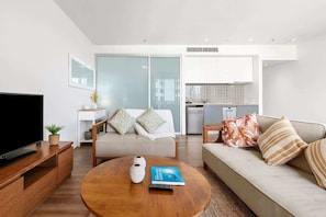 A modern living room with a TV, sofa, coffee table, and a kitchen in the background.