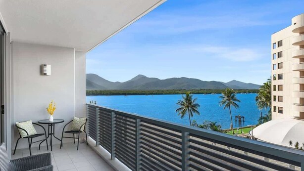 Un balcon donnant sur un plan d’eau et des montagnes, une table avec des chaises et une plante en pot.