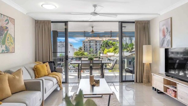 Ein modernes Wohnzimmer mit Sofa, Couchtisch, Fernseher und Balkon mit Blick auf Gebäude und Grünflächen.