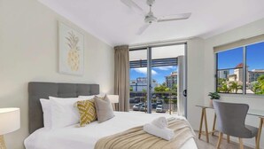 Ein Hotelzimmer mit Bett, Schreibtisch, Stuhl, Deckenventilator und einem großen Fenster mit Blick auf Gebäude und einen Parkplatz.