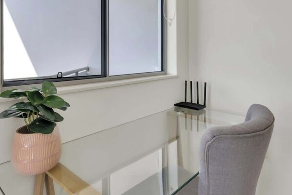 Ein Zimmer mit Glastisch, Blumentopf, grauem Sessel und einem Fenster mit Jalousien.