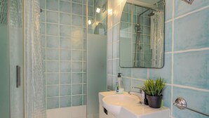 Une salle de bain avec une douche à parois de verre, un lavabo avec un miroir au-dessus et une plante en pot posée sur le lavabo.